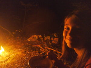 A teenager enjoying her first dinner and nigth around the fire in the woods - Adolescente souriant durant son premier dîner auprès du feu en nature
