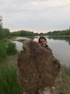 A woman showin a salted deer hide on a river bank